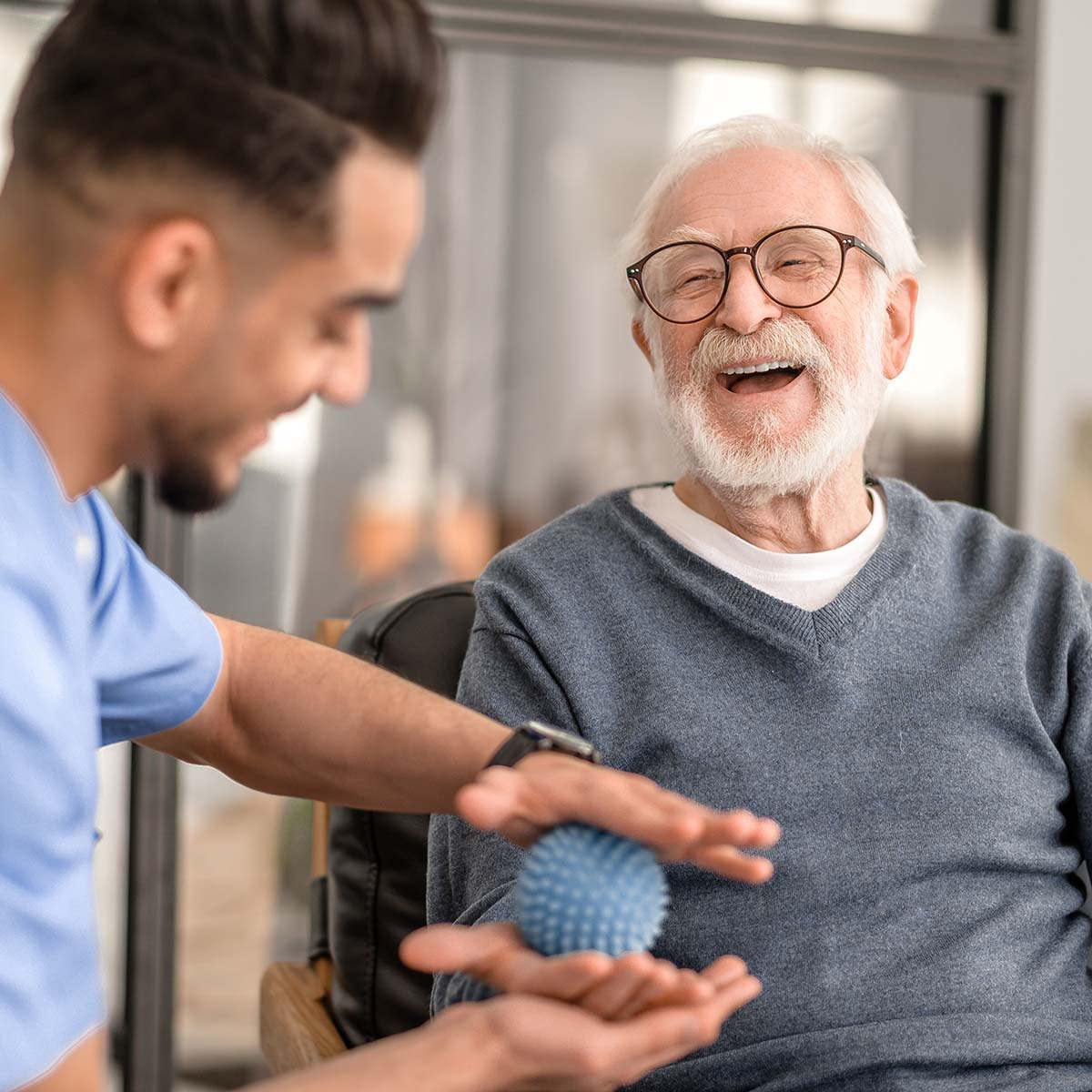 A male senior smiles as his hand is massaged.