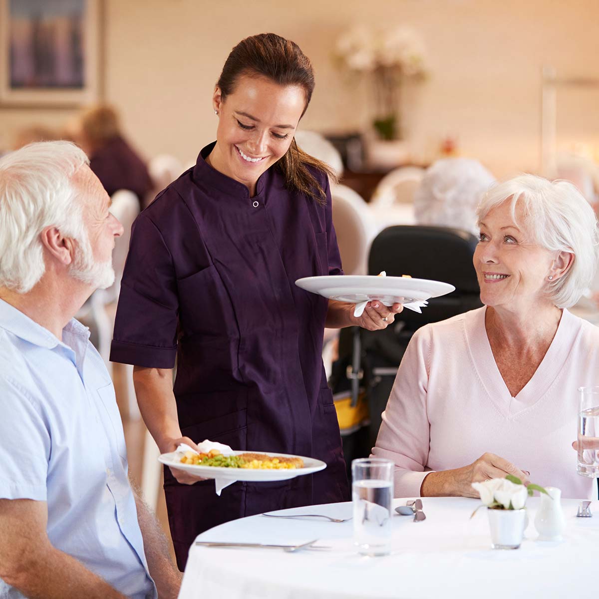 An Immanuel server sets down two plates of food for a senior couple.